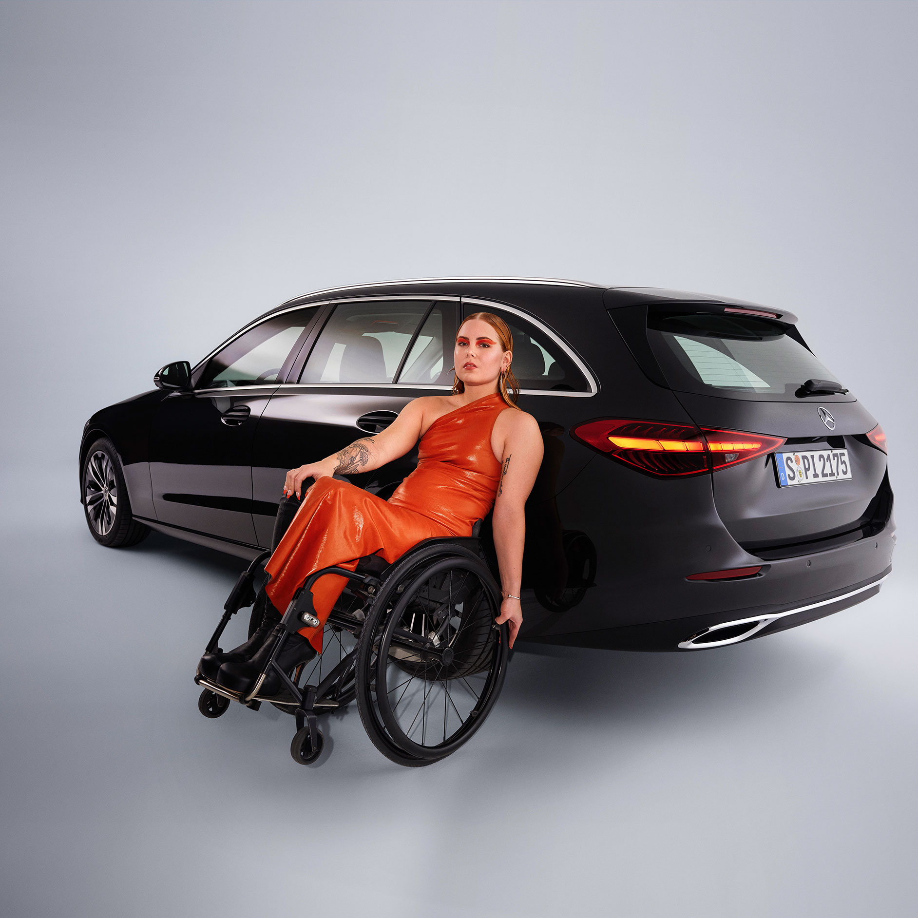 Calitate | Sisteme de asistență la rulare | Mercedes-Benz Un autovehicul adaptat persoanelor cu dizabilități - modelul Clasa C model T - într-o vedere oblică din spate și o femeie în scaun cu rotile.